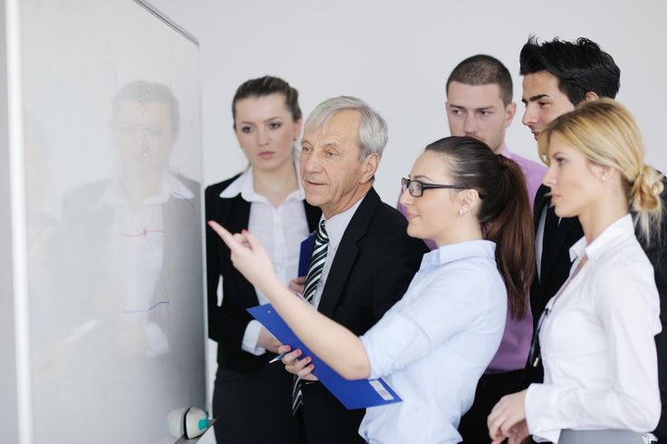 a group of business people standing in front of a whiteboard talking to each other