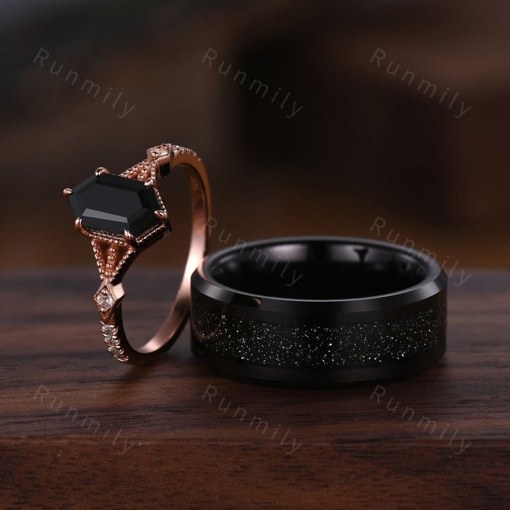 two wedding rings with black diamonds on them sitting on top of a wooden table next to each other