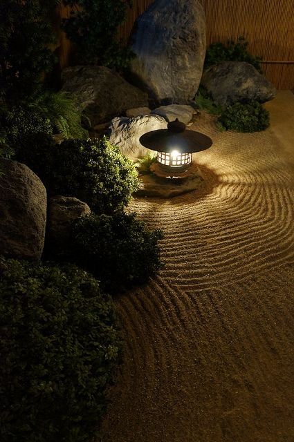 a lit lantern in the middle of a rock garden at night with rocks and grass