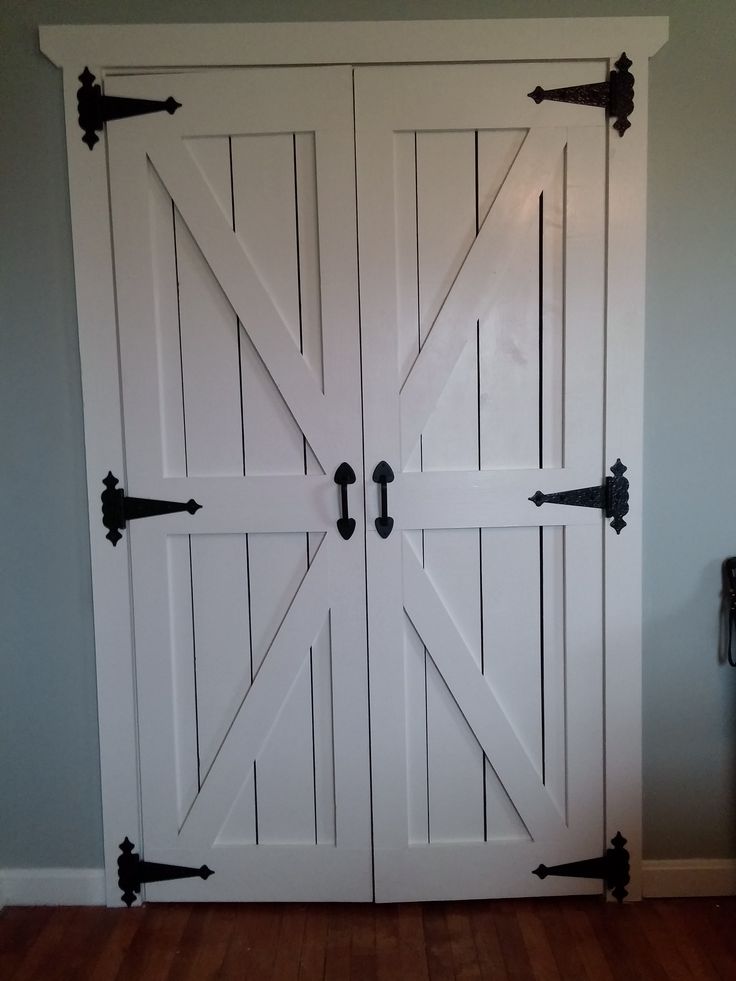 an open white barn door with black hardware on the top and bottom panel, in a room