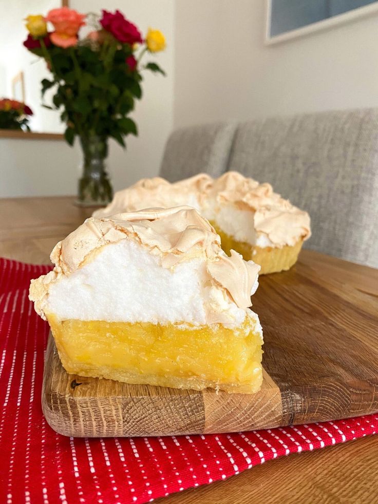 two lemon meringue pies on a wooden cutting board with flowers in the background