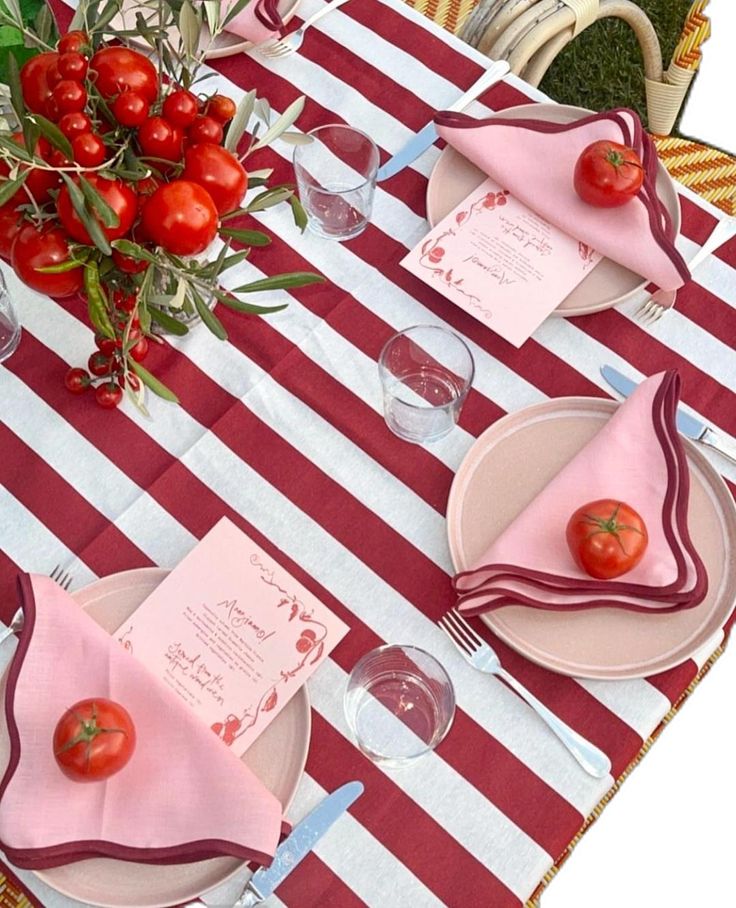 the table is set with red and white striped cloths, place mats, napkins, and tomatoes