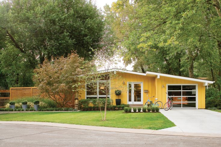 a yellow house with a bicycle parked in front of it and trees around the yard