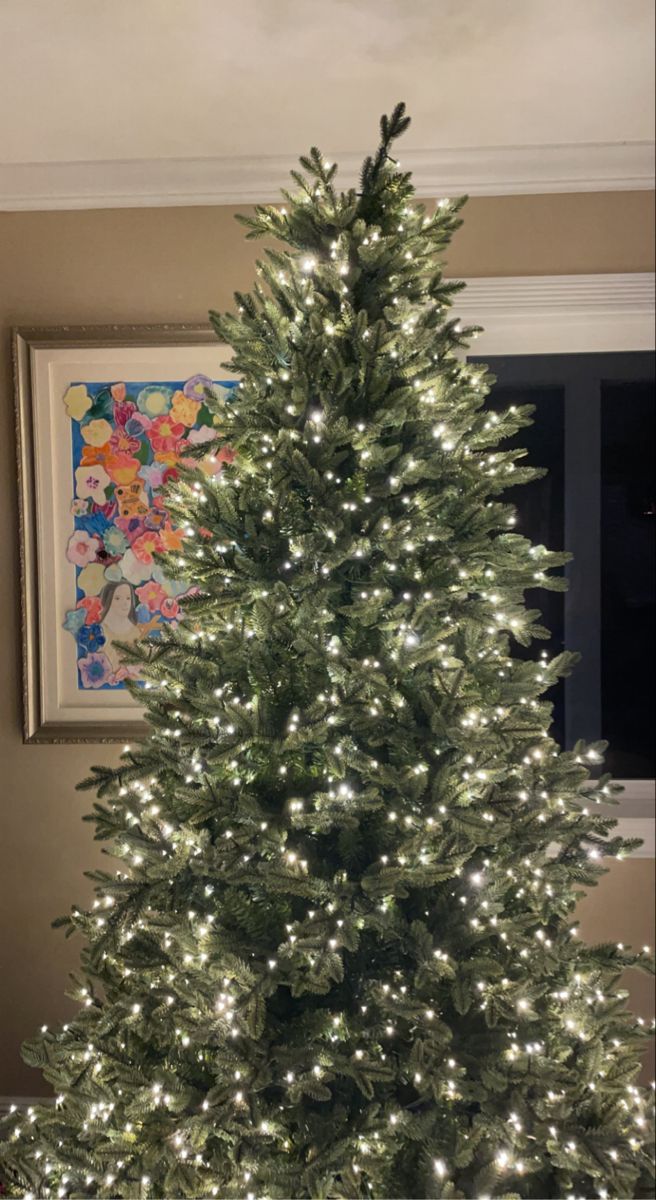 a white christmas tree is lit up in the living room with its lights on and it's green tinsel