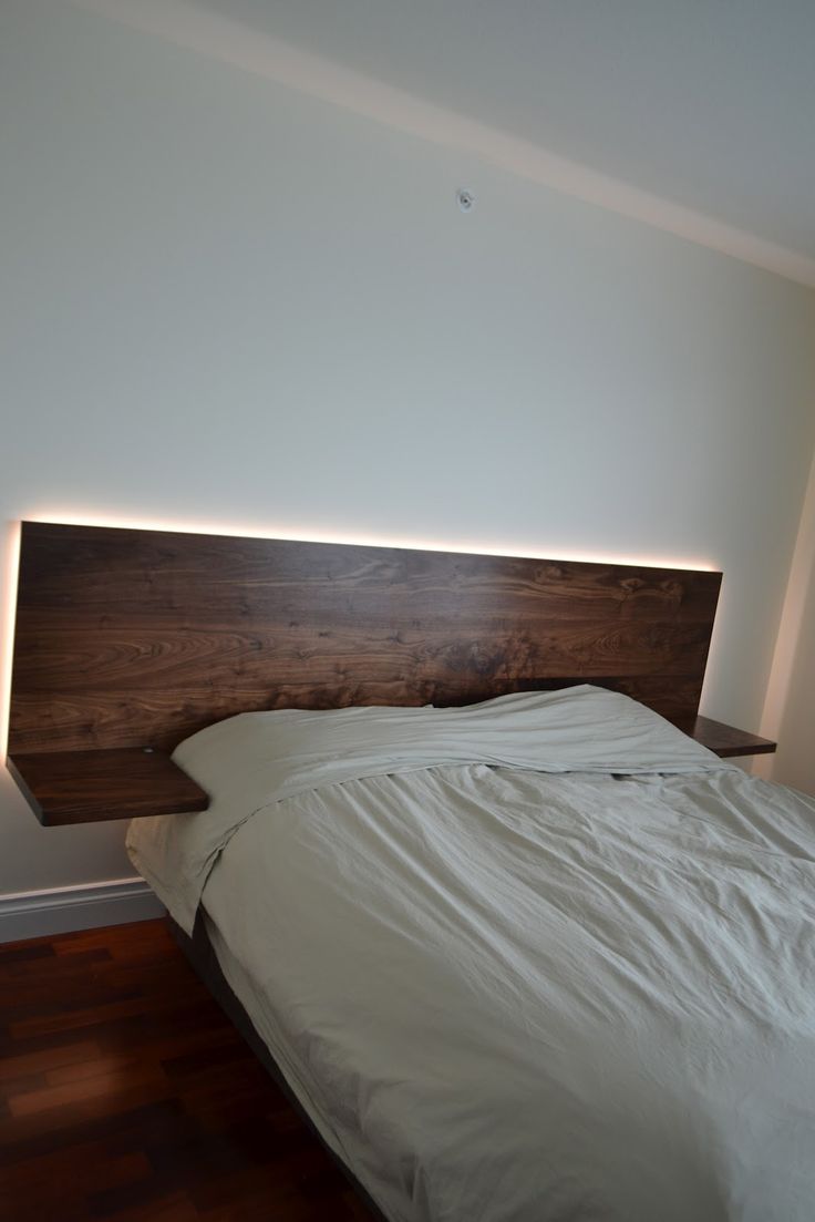 a bed with white sheets and wooden headboard in a room that has hard wood flooring