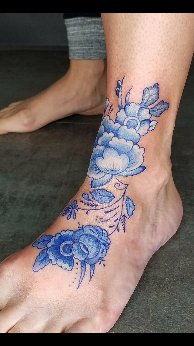 a woman's foot with blue flowers and leaves on her left side, tattoo style