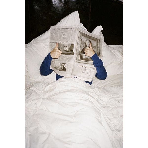 a person laying in bed reading a newspaper and pointing at the viewer with their thumb up