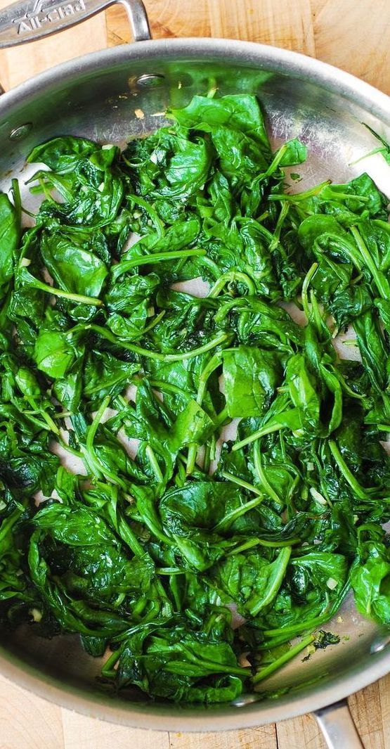 spinach and onions cooking in a pan on a wooden table with utensils