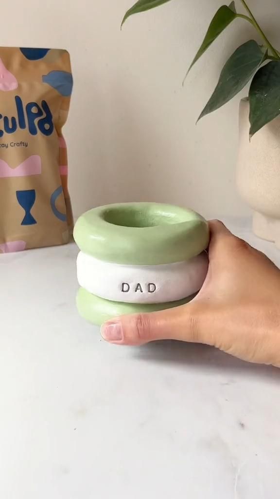 a hand holding a green and white bowl with the word dad on it next to a bag