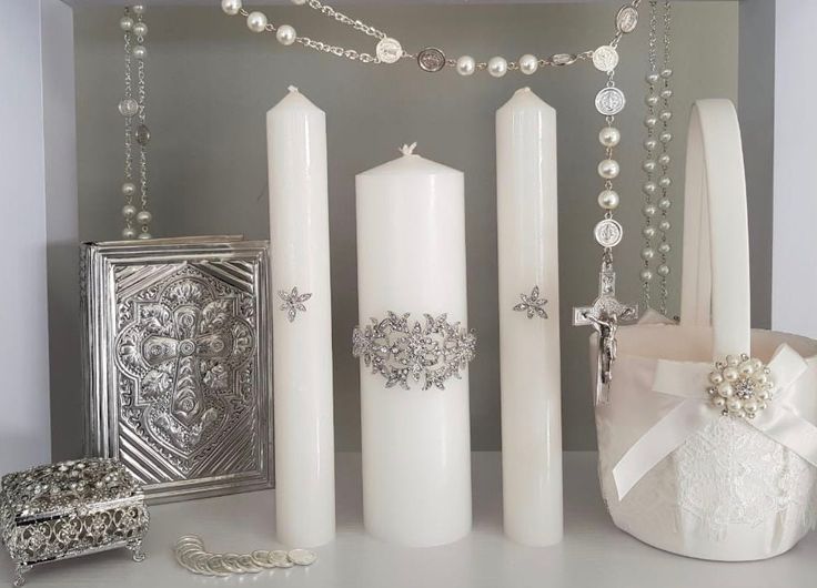 some white candles are on a table with pearls and other items around them, including a purse