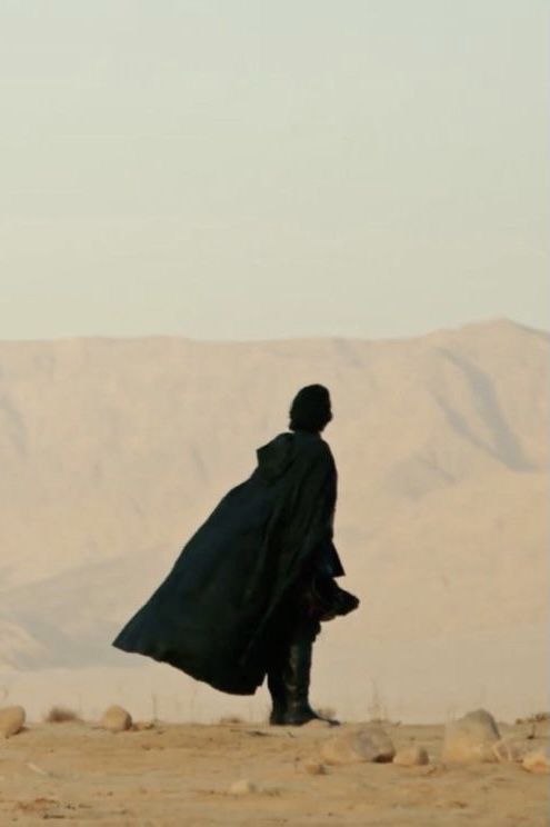 a man with a cape walking in the desert