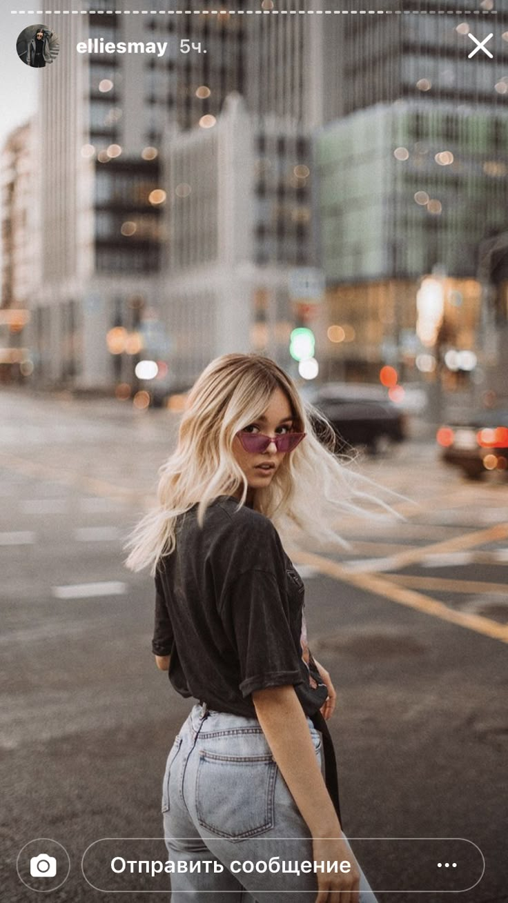 a woman with blonde hair is standing in the middle of an empty street and looking at her cell phone