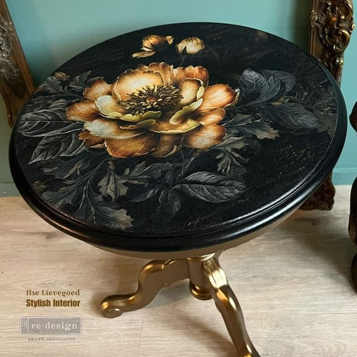 a black and gold table with flowers painted on the top, sitting in front of a blue wall