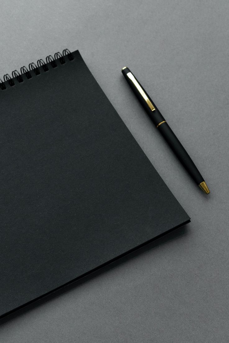 a black notebook and pen on a gray surface