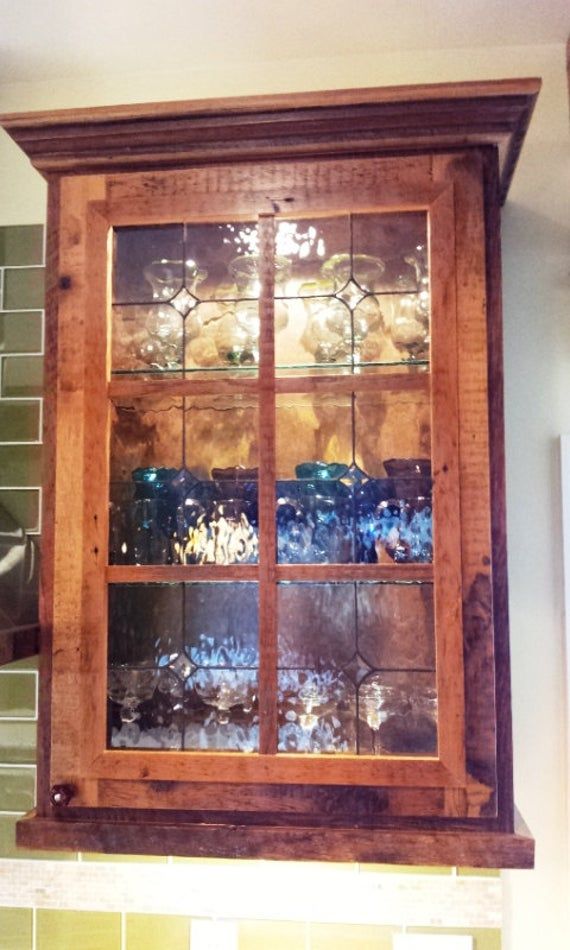 a wooden cabinet with glass doors on the top and bottom, in front of green tiles