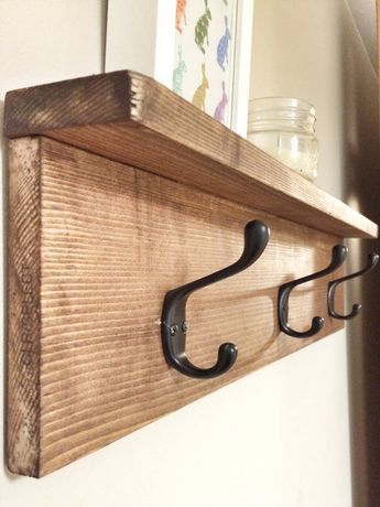 a wooden shelf with two black metal hooks and a mason jar on the wall behind it