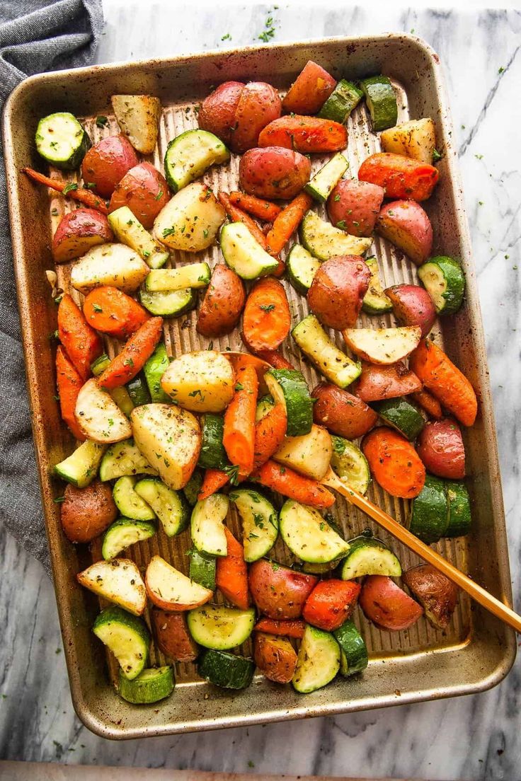 roasted vegetables in a baking pan with a wooden spatula