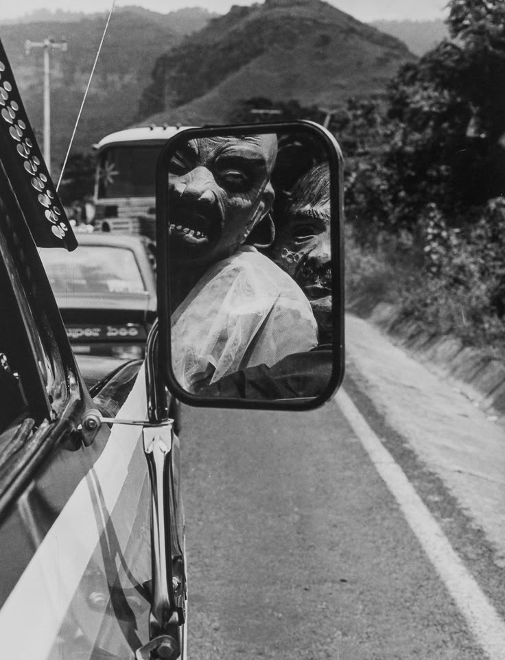 a black and white photo of a car's rear view mirror with the reflection of a person in it