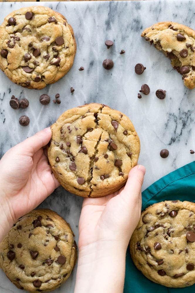 chocolate chip cookies are being held by someone's hand on a marble countertop