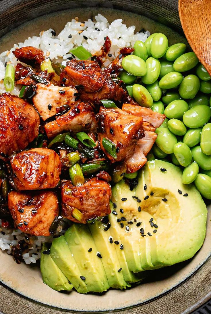 a bowl filled with rice, meat and vegetables next to an avocado slice