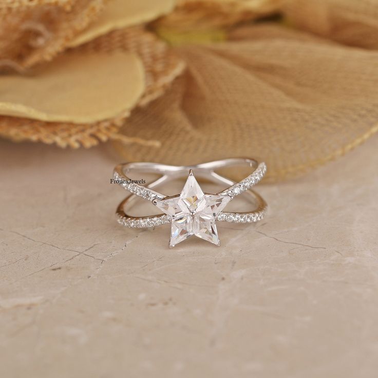 a white gold ring with a star shaped diamond in the center on a beige background