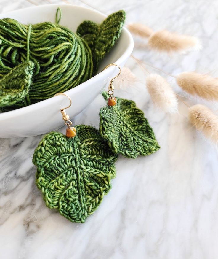 green leaf shaped earrings sitting on top of a counter next to some feathers and yarn