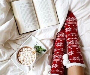 a woman laying in bed with her legs crossed and reading a book