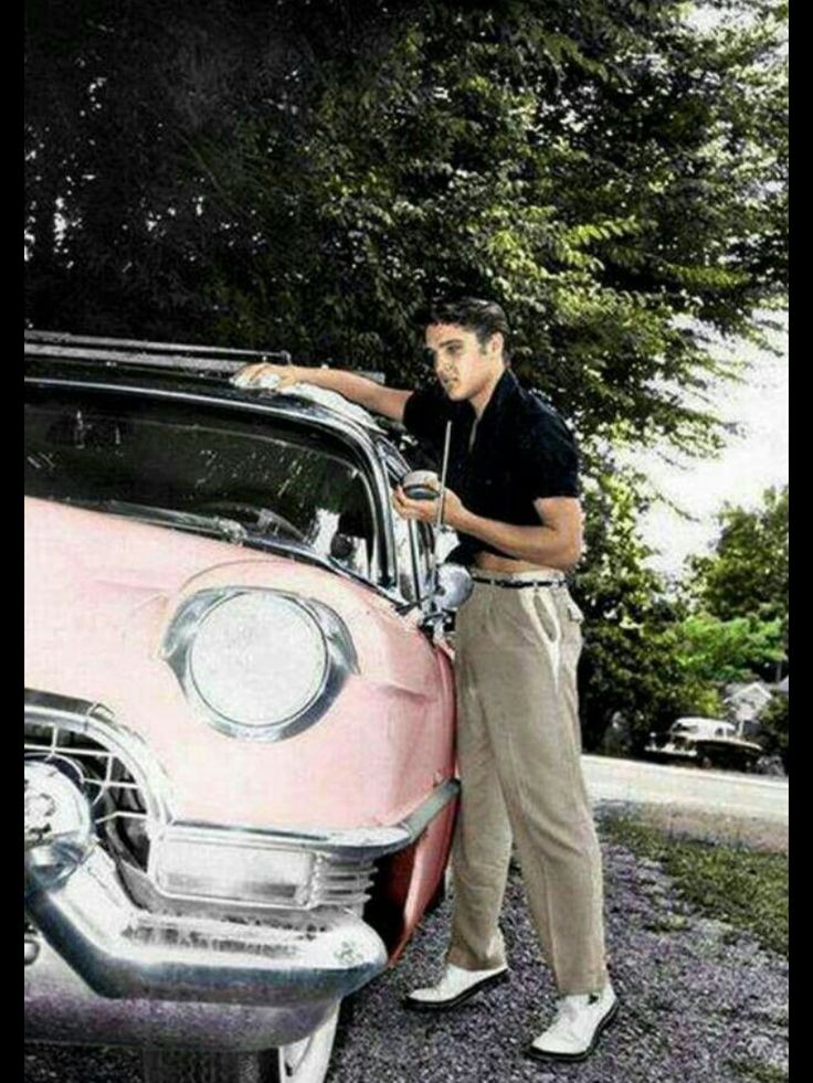 a man standing next to an old pink car