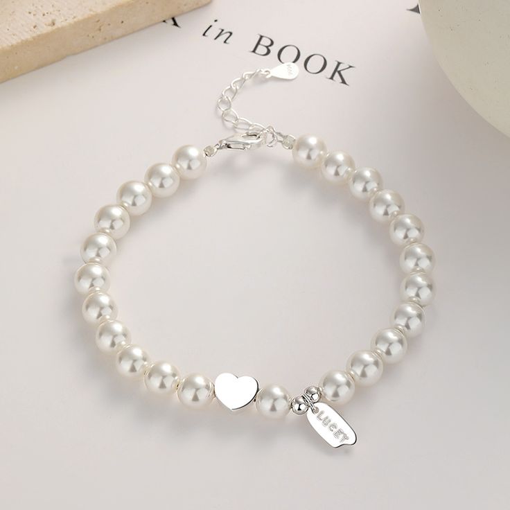 This stunning piece features a delicate strand of lustrous pearls, gracefully encircling your wrist. Nestled in the center, a shimmering silver heart adds a touch of romance, while a finely crafted pendant, engraved with the word "lucky," dangles gracefully, radiating positive energy. Adorn yourself with this timeless treasure, as it embodies the essence of beauty and fortune. Each pearl represents the wisdom gained from life's precious moments, while the silver heart symbolizes love and compass Silver Heart-shaped Jewelry With Pearl Charm, Silver Heart-shaped Pearl Jewelry, Elegant Charm Bracelet For Anniversary, Heart Shaped Silver Jewelry With Pearl Chain, Elegant Sterling Silver Jewelry With Heart Beads, Dainty Silver Bracelet With Pearl Chain, Valentine's Day Silver Jewelry With Pearl Chain, Valentine's Day Silver Pearl Chain Jewelry, Elegant Anniversary Charm Bracelet