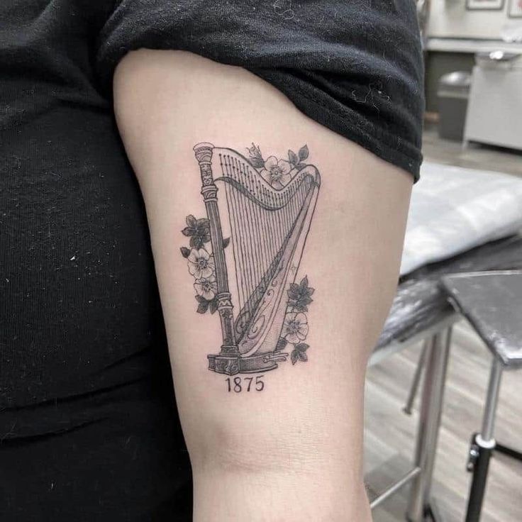 a woman's arm with a tattoo on it that has a harp and flowers