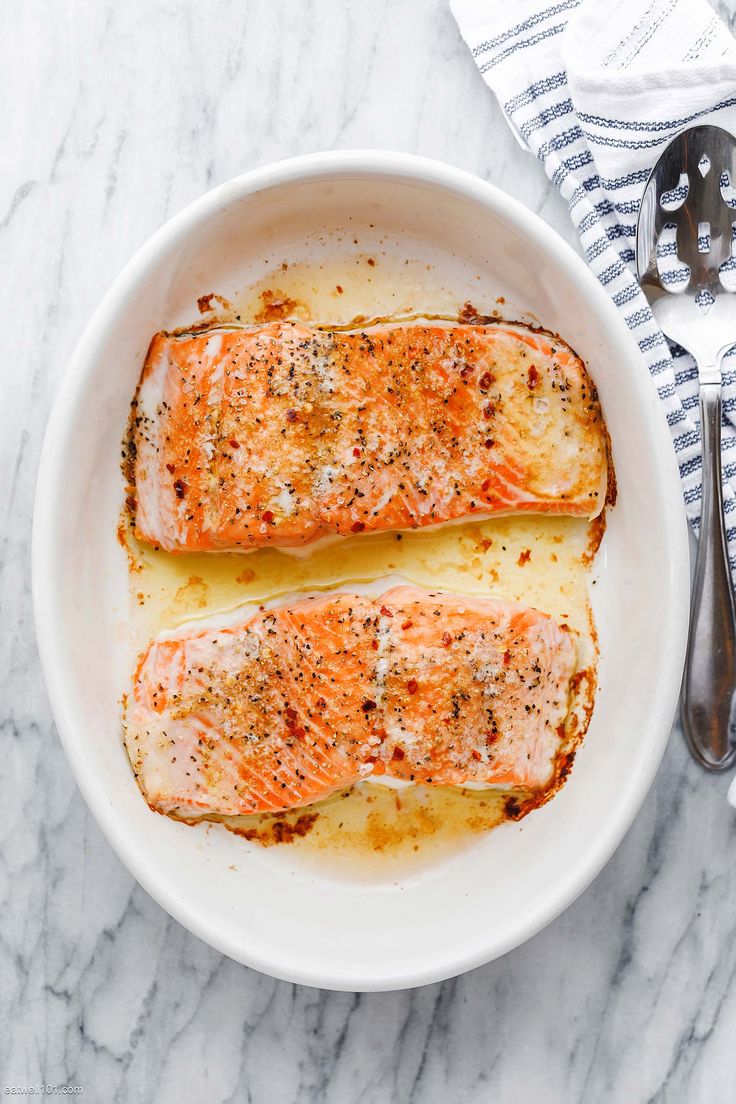 two salmon fillets in a white bowl on a marble counter top with spoons