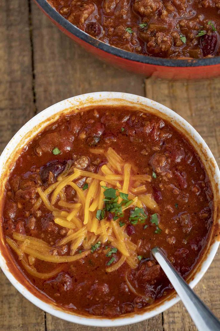 two bowls filled with chili and cheese on top of a wooden table