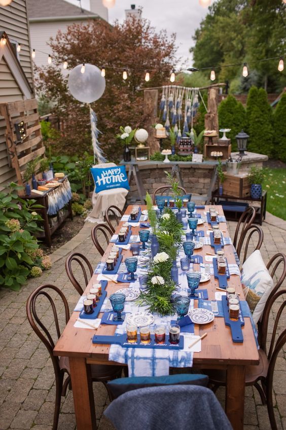 a long table with blue and white plates on it in the middle of a yard