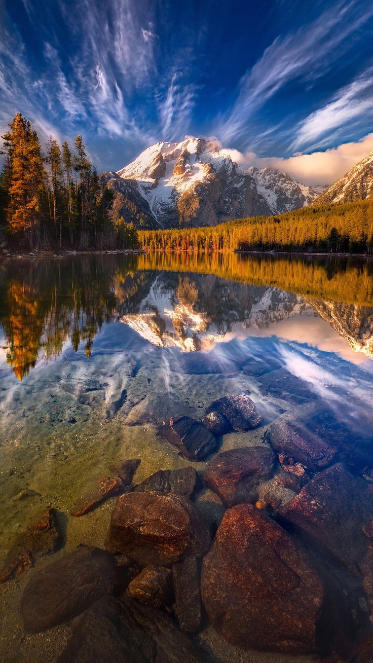 the mountain is reflected in the still water on the lake's shore, with rocks and trees around it