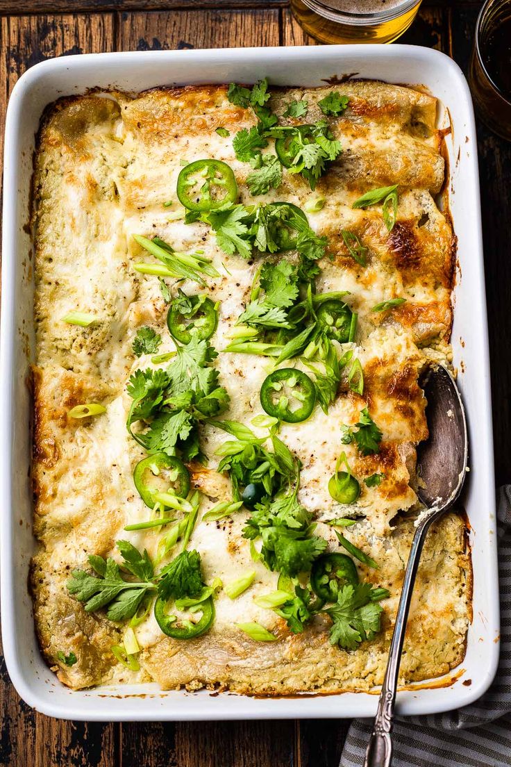 a casserole dish with green vegetables and cheese on top, next to a glass of beer