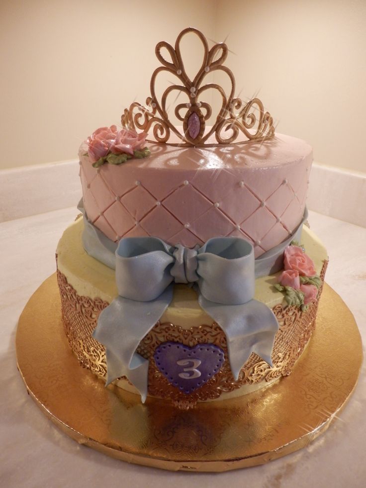 a three tiered cake decorated with pink and blue frosting, gold trimmings and bows