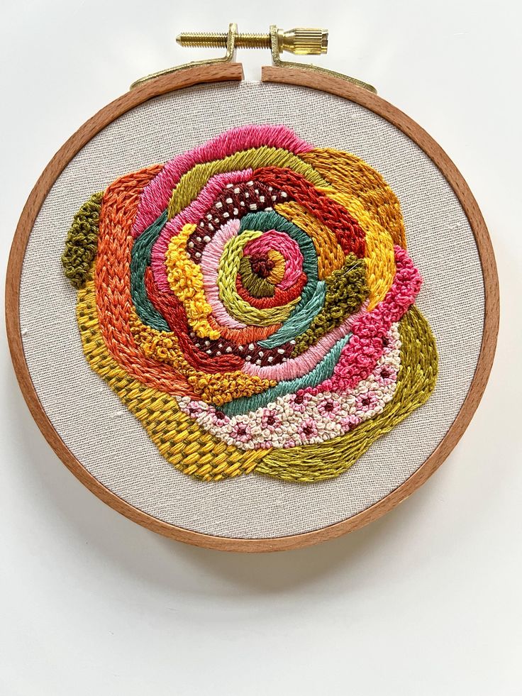 a close up of a embroidery on a white surface with a wooden hoop holding an embroidered flower