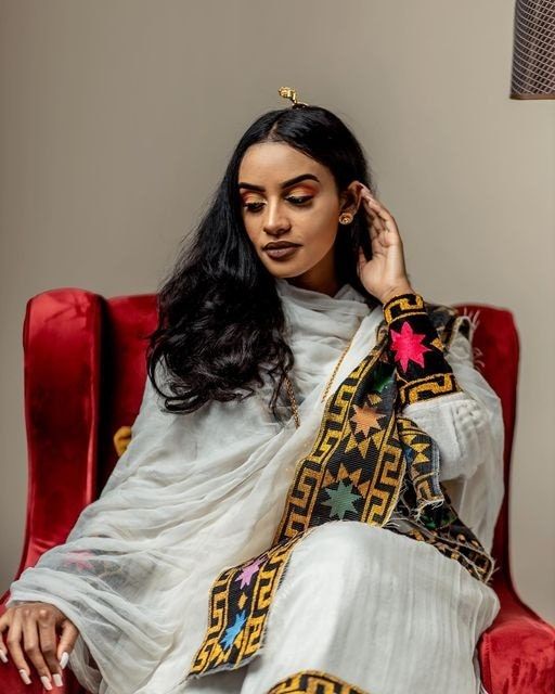 This Shimena Ethiopian traditional dress is a true masterpiece that embodies timeless elegance and sophistication. The dress is made with high-quality Menen fabric, which adds a touch of luxury and refinement to the overall design. The dress features a wide Tilf design that adds a traditional charm to the modern silhouette. The dress is designed to fit comfortably and flatteringly, with a fitted bodice and a full skirt that flows beautifully as you move. The dress is complemented by carefully se Ethiopian Dress Modern, Eritrean Women, Eritrean Clothing, Eritrean Dress, Beautiful Ethiopian, Ethiopian Clothing, Habesha Dress, Ethiopian Traditional Dress, Ethiopian Dress