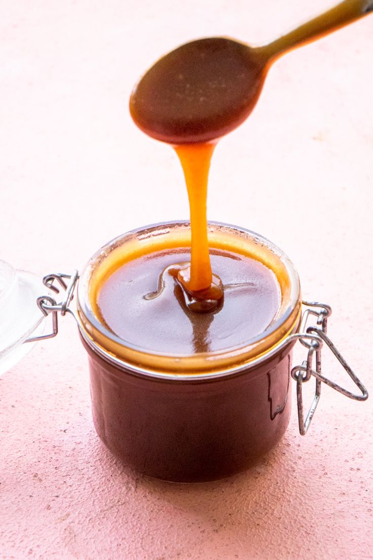 a spoon is pouring caramel sauce into a jar