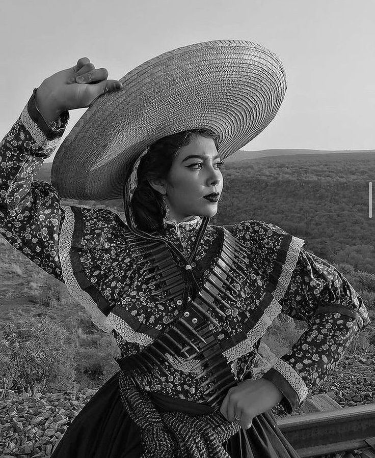 a woman wearing a large hat standing on top of a wooden bench next to a field