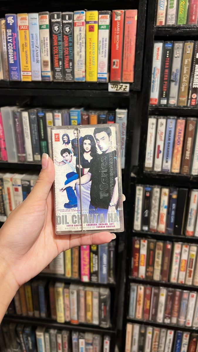 a person holding up a dvd in front of a shelf full of dvds