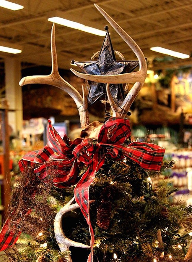 an antlers head on top of a christmas tree with red and black ribbon around it