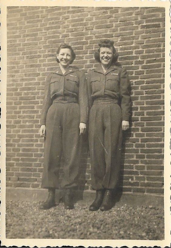 two women are standing next to each other in front of a brick wall and wearing uniforms