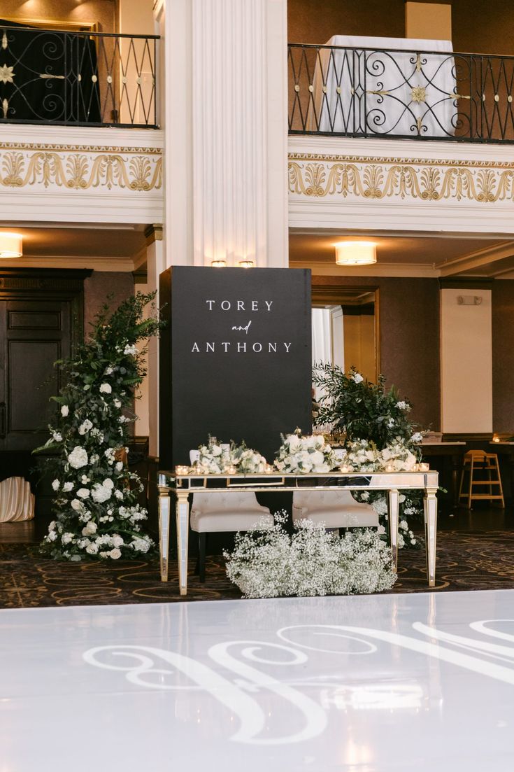 a sign that is sitting in the middle of a room with flowers and greenery