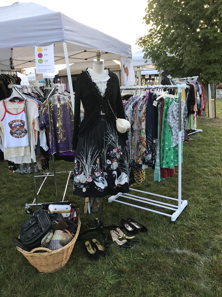 clothes and shoes are on display at an outdoor flea market in the grass under a tent