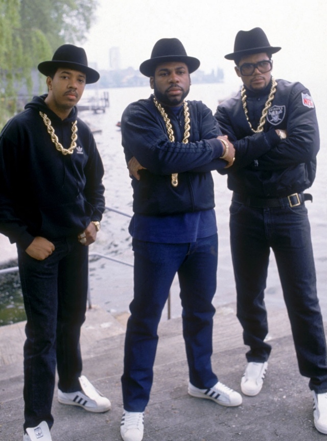 three men in black hats and chains standing next to each other near the water with their arms crossed