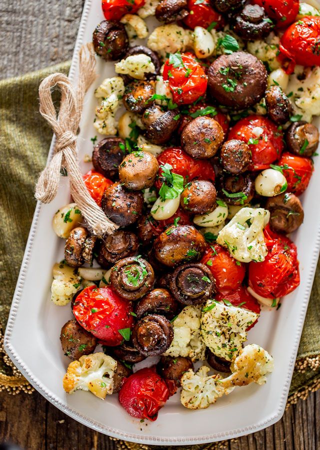 a platter filled with mushrooms, tomatoes and cauliflower on top of a wooden table