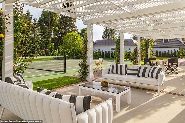 an outdoor living area with couches, tables and tennis court