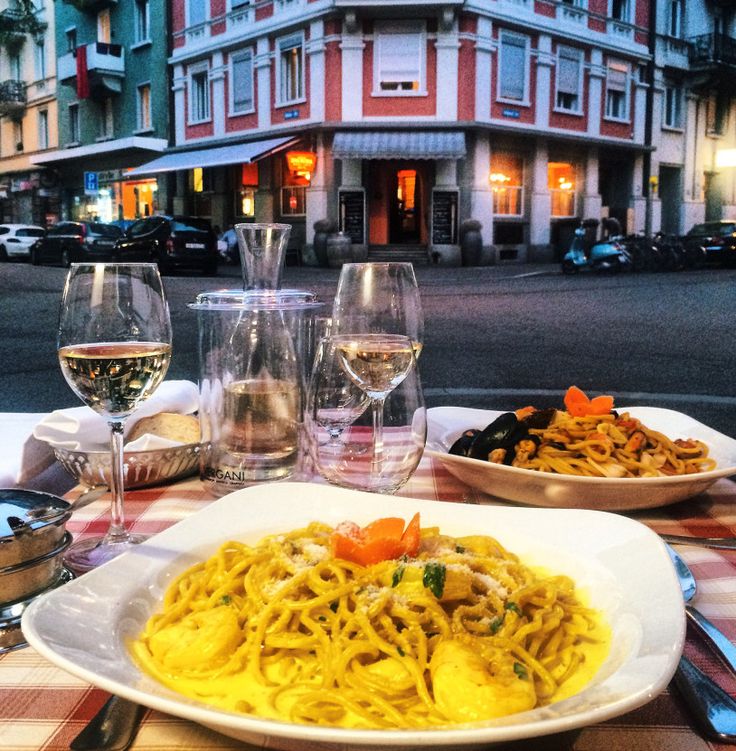 two plates of pasta and wine on a table in front of a building at night