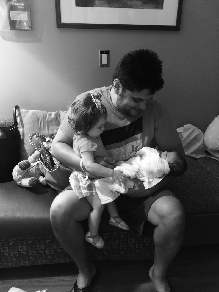 a man holding a baby while sitting on top of a couch next to a woman